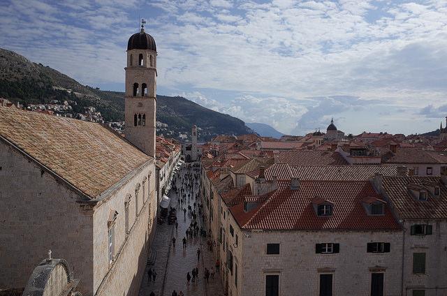 Dubrovnik (c) worldaroundtrip by creative commons Vanuit de lucht zien we wandelaars tussen de lichtgekleurde huizen en de torens. Op de achtergrond, de bergen.