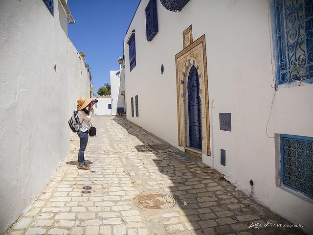 Tunis (c) Dominique Touel by creative commons Een toerist fotografeert de helblauwe deur van een wit huis in een zonovergoten straatje in Tunis.