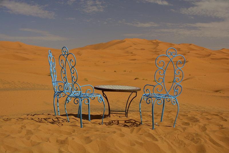Waiting for our green tea (c) Antonio Cinotti by creative commons Twee sierlijke azuurblauwe stoelen en een rond tafeltje staan klaar voor de thee in een woestijnlandschap.