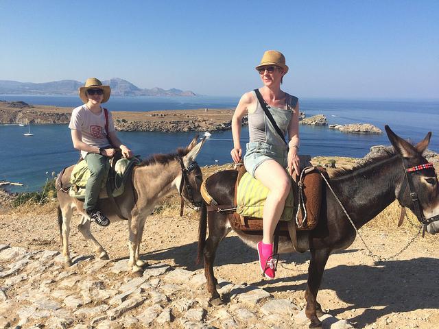 Riding up to the Lindos Acropolis, Rhodes (c) tracy the astonishing by Creative Commons Twee vrouwen (niet Monique) rijden met de ezel door een rotsig landschap, met de zee op de achtergrond.