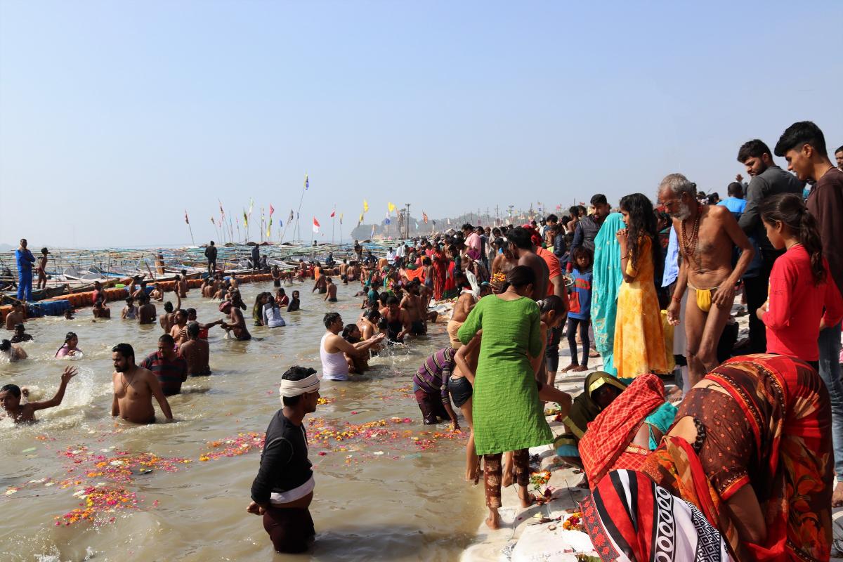 Hindoe's baden in de heilige  rivier tussen in het water uitgestrooide bloemen. Aan de kant wachten velen op hun beurt.