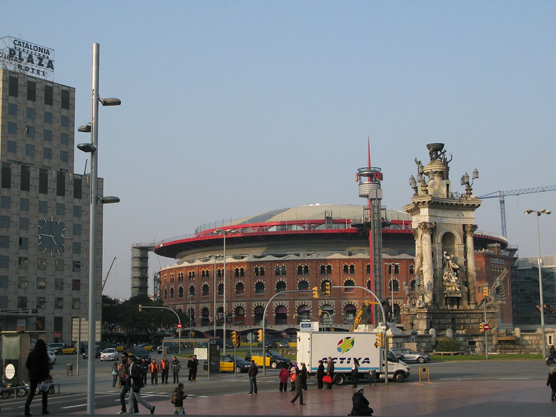 De arena is een rood, rond gebouw, ervoor prijkt een monument met verschillende zuilen en standbeelden.