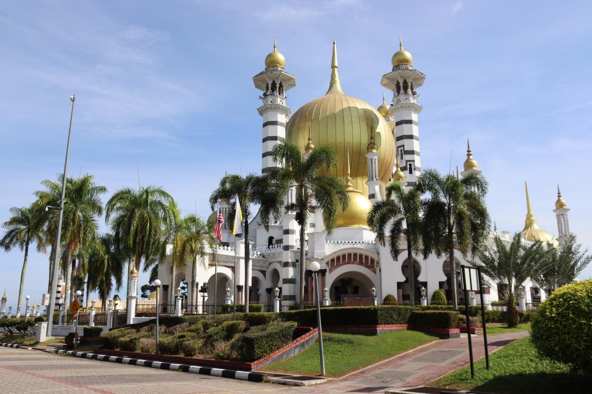 Een moskee met gouden koepels en minaretten, omgeven door kokospalmen.