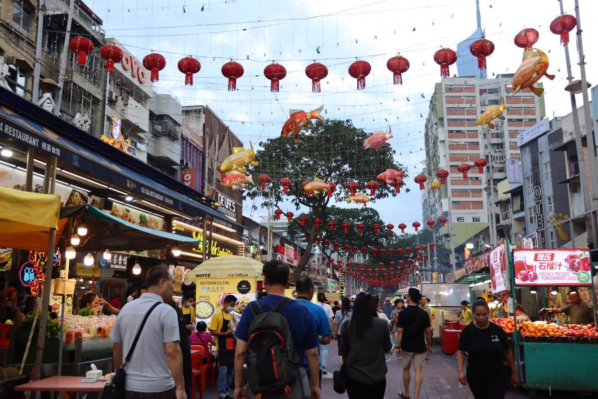 Gezellige drukte tussen de eet- en drankstandjes in Jalan Alor. Boven de straat hangen rode lampions.