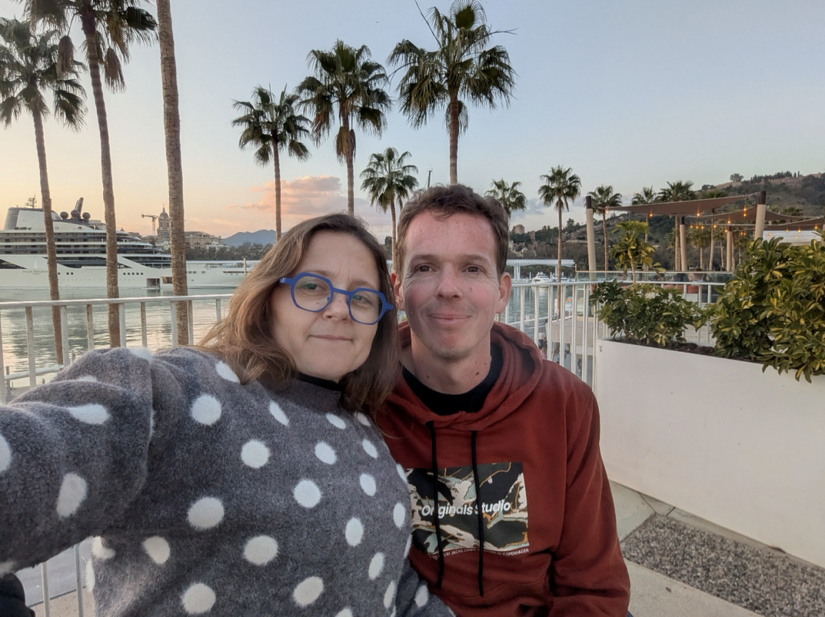 Lien en Thomas poseren samen bij de palmbomen van Malaga. Op de achtergrond zien we een stukje van de stad en een cruiseschip.