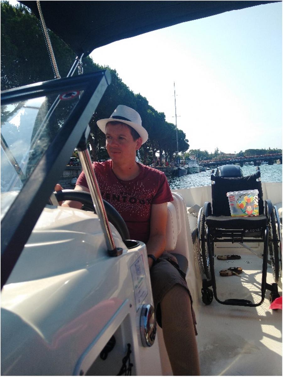 Thomas bestuurt de motorboot op het meer. Achter hem staat zijn rolstoel.