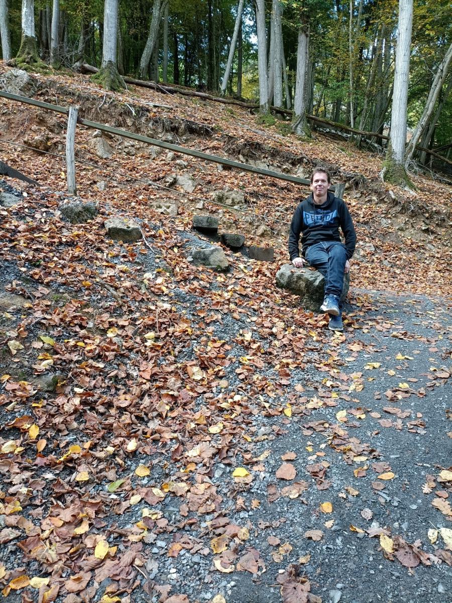 Thomas poseert in het herfstlandschap, zittend op een grote steen, met achter zich de vrij steile trapleuning.