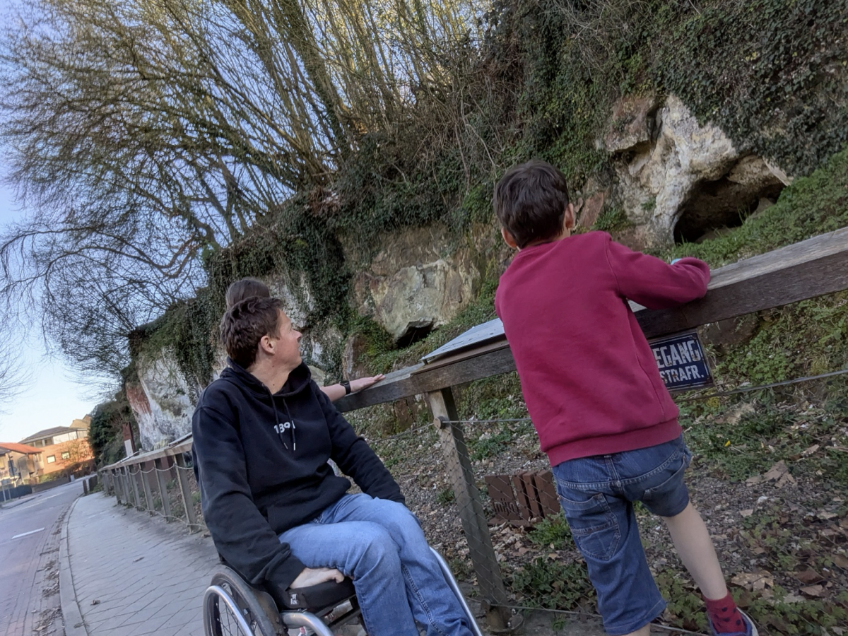 Vader met rolstoel kijkt samen met zijn zoontje over een omheining naar de rotsen.